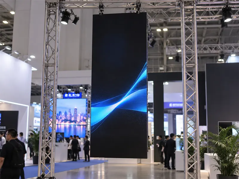 Close-up of LED poster truss mount showing half-coupler clamp on aluminum truss chord and safety cable attachment to independent chord