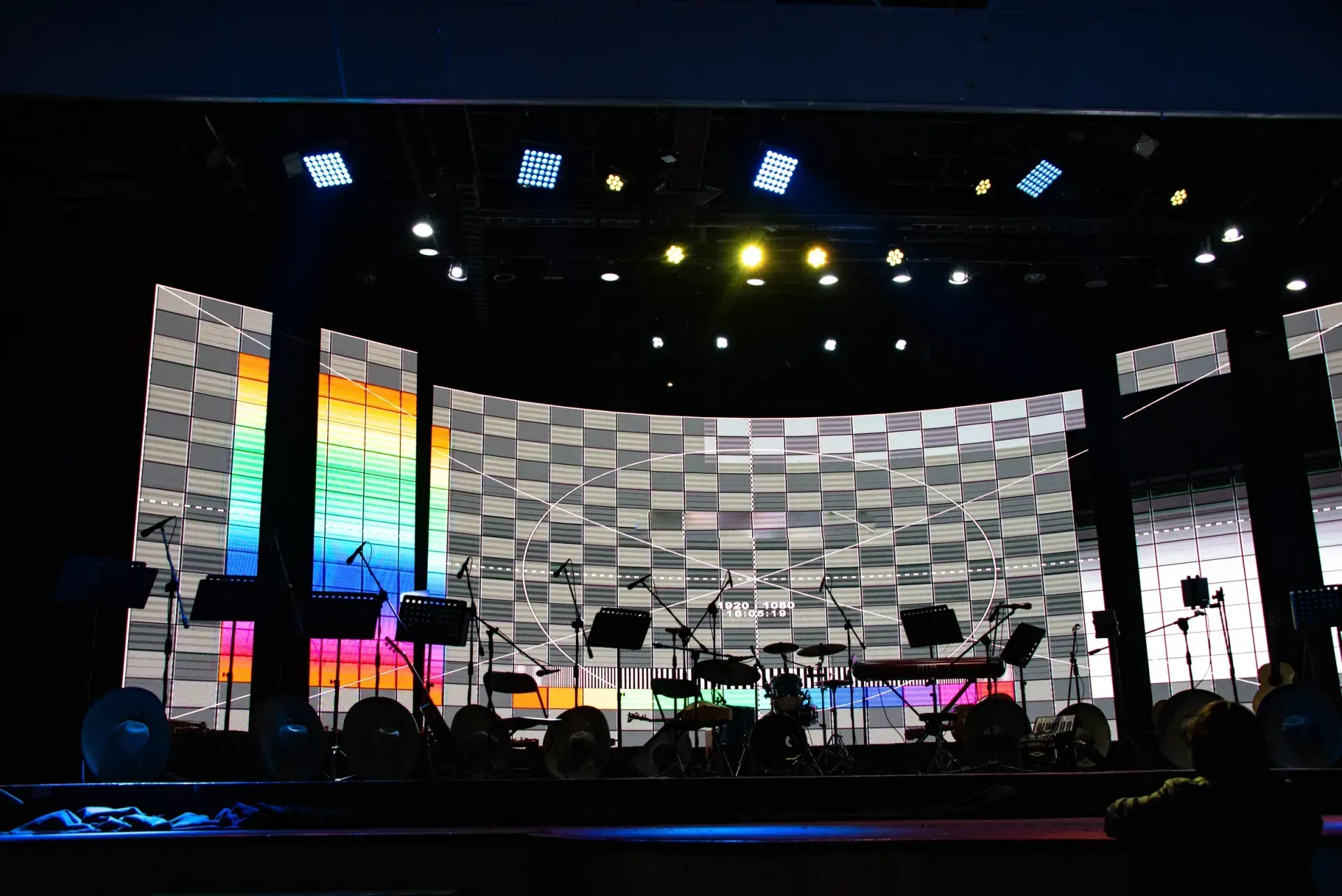Curved LED stage backdrop displaying test patterns behind musical instruments and microphones